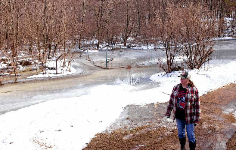 Tessa Dyer stands in her backyard that is unrecognizable under the water and ice that has engulfed her property in Loudon, off of Route 106 on Wednesday, January 10, 2024.