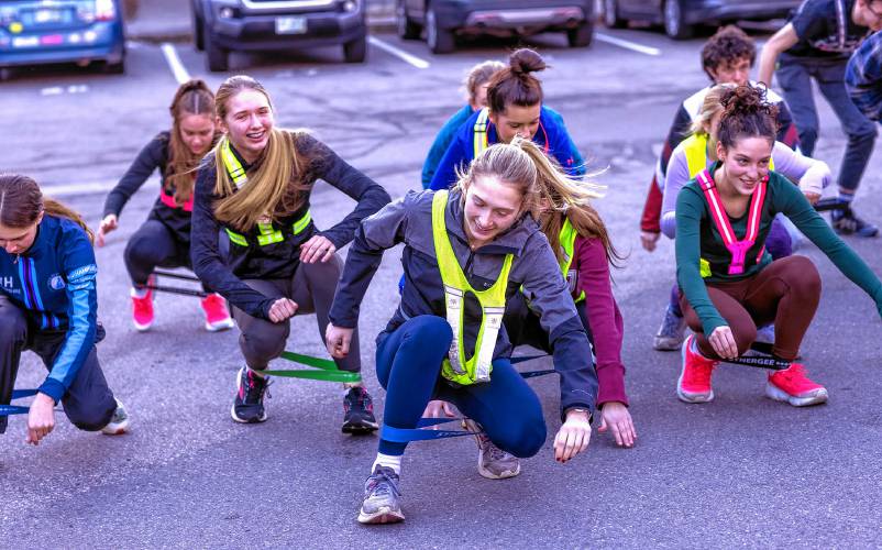 Nordic ski team captain Chloe Gudas (center) leads the team in a crab walk with bands as the members warm up in the Concord High parking lot before going a 45-minute run on Friday.
