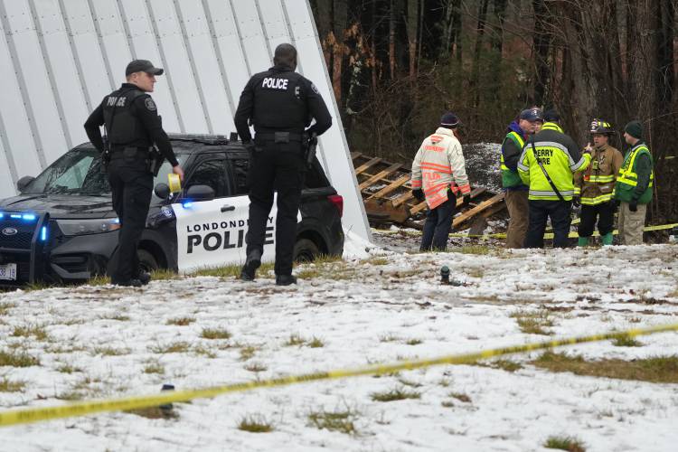 Firefighters confer near the site of a small plane crash in a wooded area behind a home, Friday, Jan. 26, 2024, in Londonderry, N.H. The Wiggins Air Beechcraft 99, which was flying light cargo to Maine, crashed about 7:30 a.m. near the Manchester-Boston Regional Airport shortly after takeoff. Firefighters helped remove the trapped pilot, who was taken to a hospital, authorities said Friday. (AP Photo/Charles Krupa)