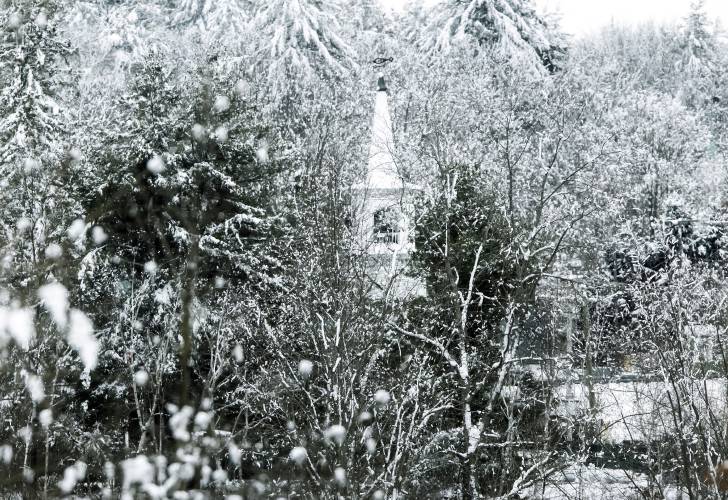 The steeple from the Congregational Church of Hooksett peeks through the weighted-down trees from the recent storms on Tuesday, January 30, 2024. The downtown view is from Lambert’s Park along the Merrimack River,