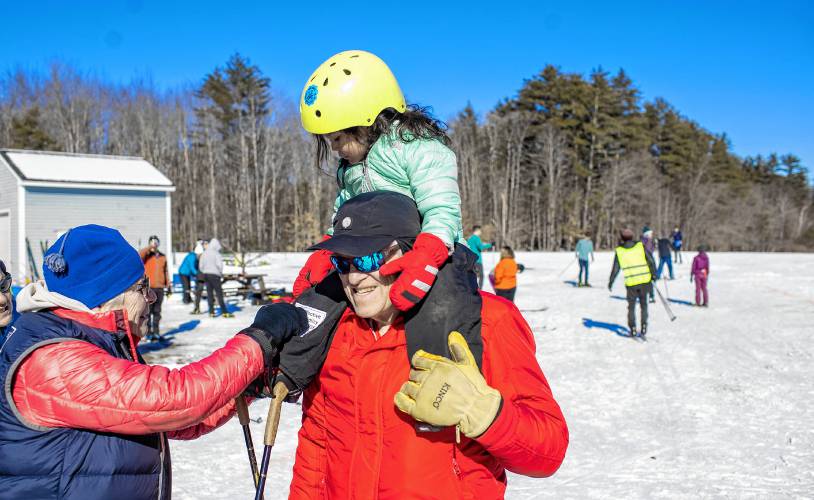 Keith Nelson holds up his granddaughter Mai, 3, as her grandmother Eliza Evans says hello after the trio finished Mai’s crosscountry lesson at The Concord Community Nordic Trails at Beaver Meadow Golf Course on Sunday, February 4, 2024. The Sunday event paired a low-key freestyle community citizens race with a free Learn-to-Ski clinic for those new to the sport.
