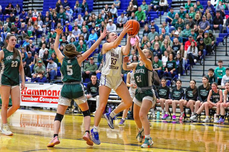 Lilli Carlile (33) splits between Pembroke’s Anne Phillips (5) and Taylor Renna as she drives to the basket during the Division II girls’ basketball championship at UNH on Sunday.