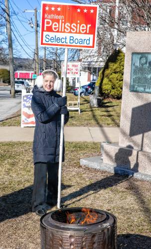 Kathleen Pelissier stands behind a small heater as greets voters in front of the St. John’s Parish Hall in Allenstown on Tuesday, March 12, 2024.